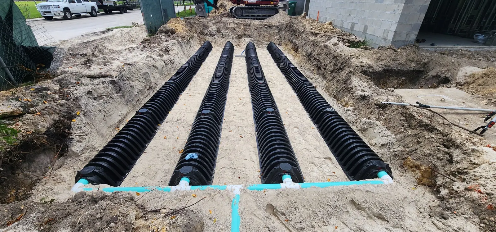 Four black corrugated chambers in a sand trench with teal pipe